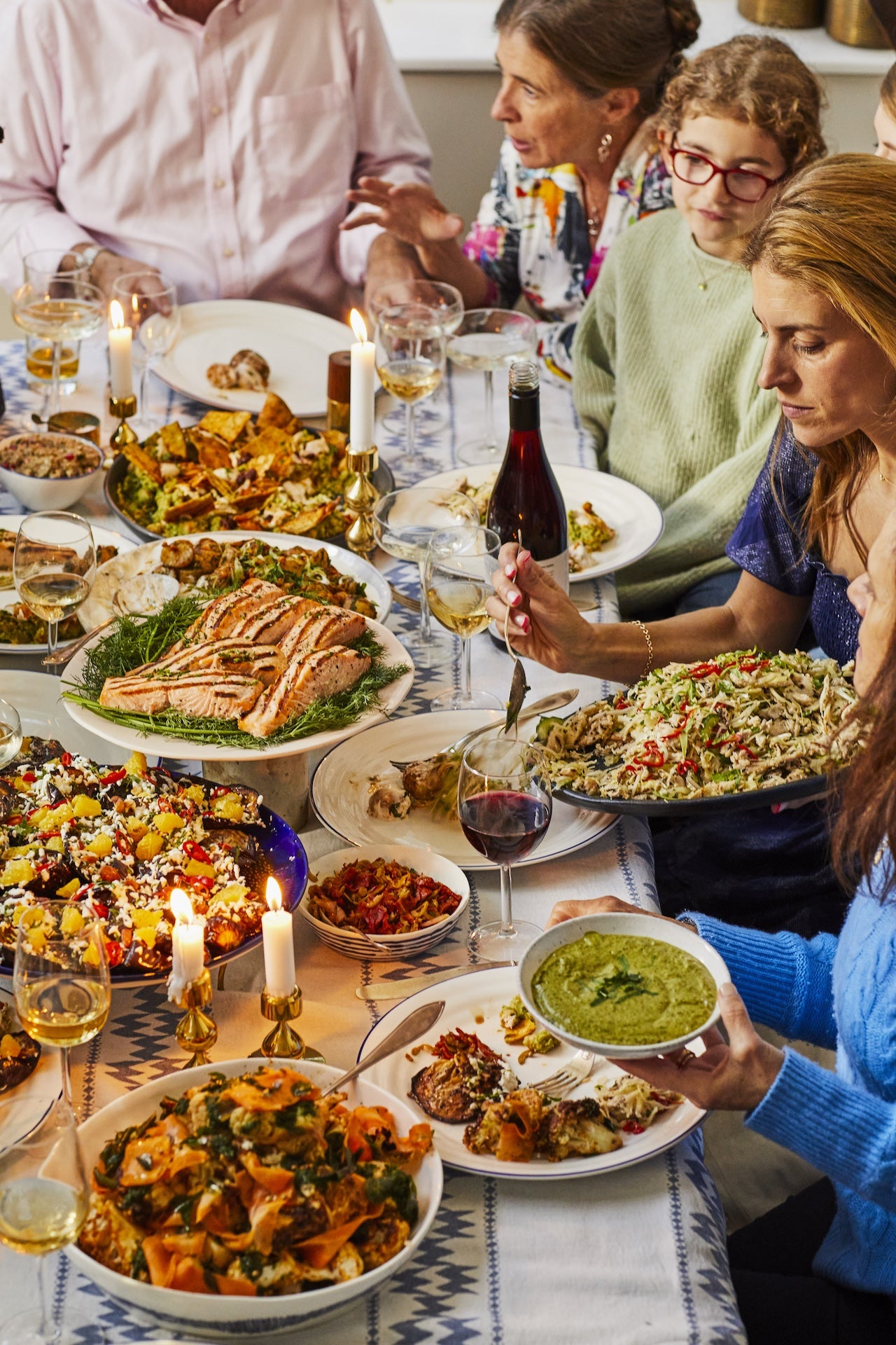 A dinner table with salad and salmon platters with a family eating the meal.