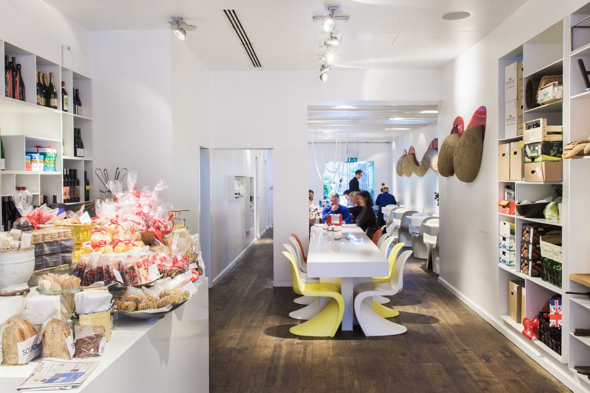 Restaurant interior, with lond sharing table in the middle, product display on the left and shelfs with produce