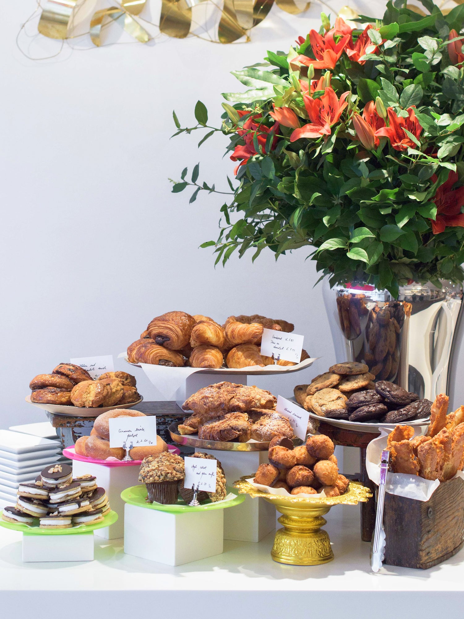 Pastry display with platters of: s'mores, viennoiserie, macaroon and cookies. Big vase of flowers at the background
