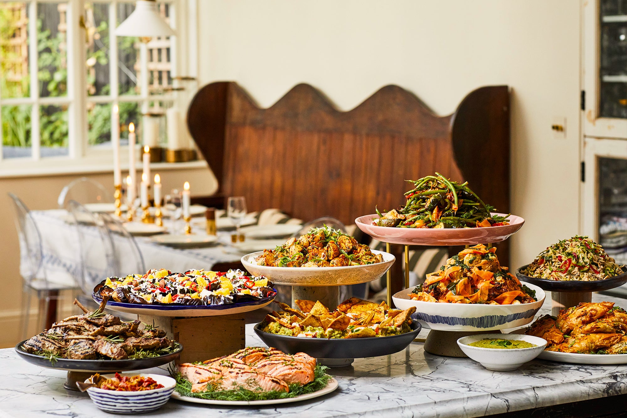 A display of big platters with salads: courgette, salmon, chicken, aubergine green beans. Dinner table at the back