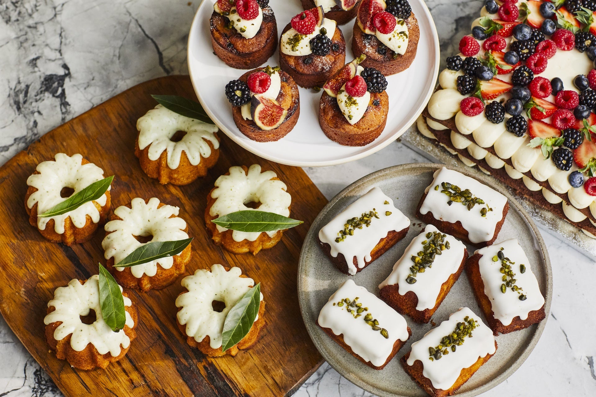 Platters with cakes: vanilla financier with berries and figs, Sicilian lemon and bay leaf teacake, flourless lemon polenta cake, celebration cake